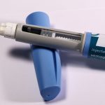 Caneta de aplicação de medicamento sobre fundo neutro.