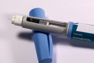 Caneta de aplicação de medicamento sobre fundo neutro.