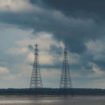 Duas torres de transmissão de energia junto a um rio sob nuvens carregadas de chuva.