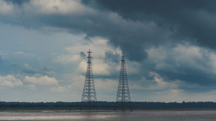 Duas torres de transmissão de energia junto a um rio sob nuvens carregadas de chuva.
